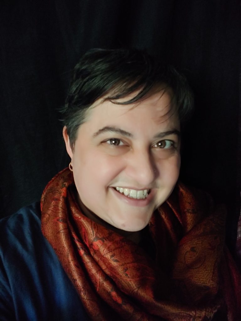 portrait photo of Leela Sinha wearing a scarf against a dark background.