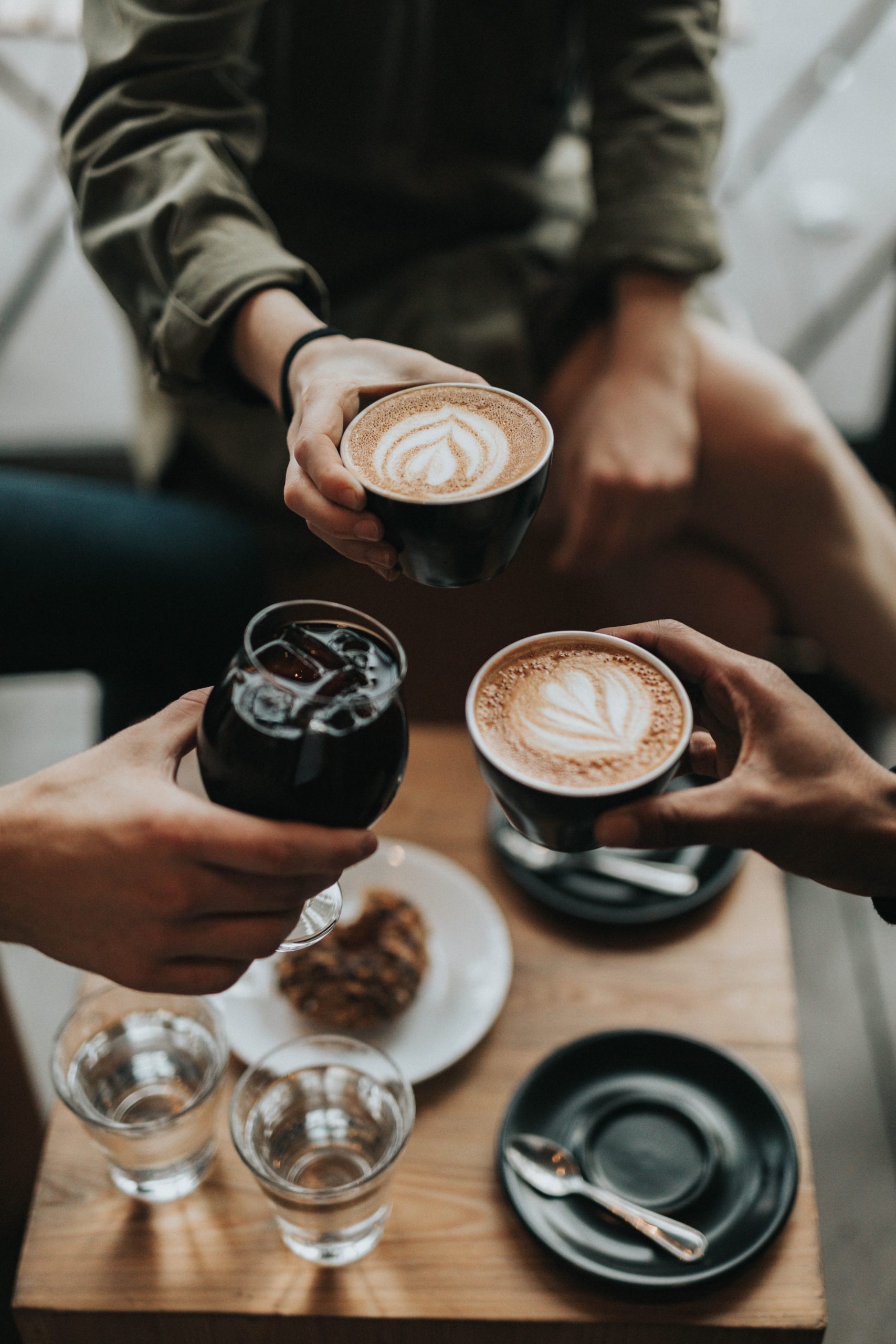 three people's hands holding coffee and other drinks raised in a toast to one another